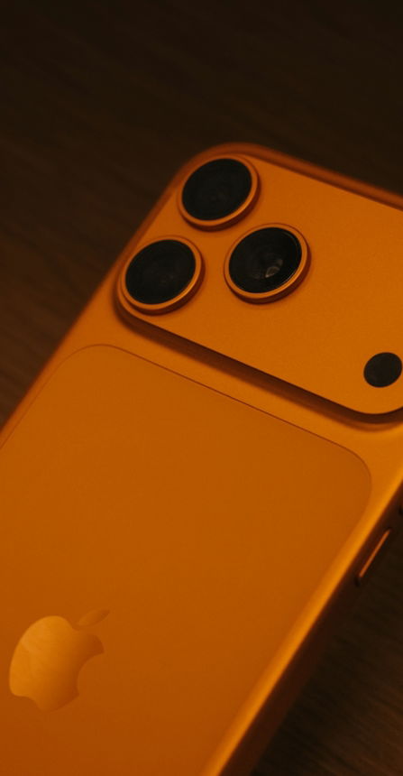 Back of an orange smartphone with three cameras.